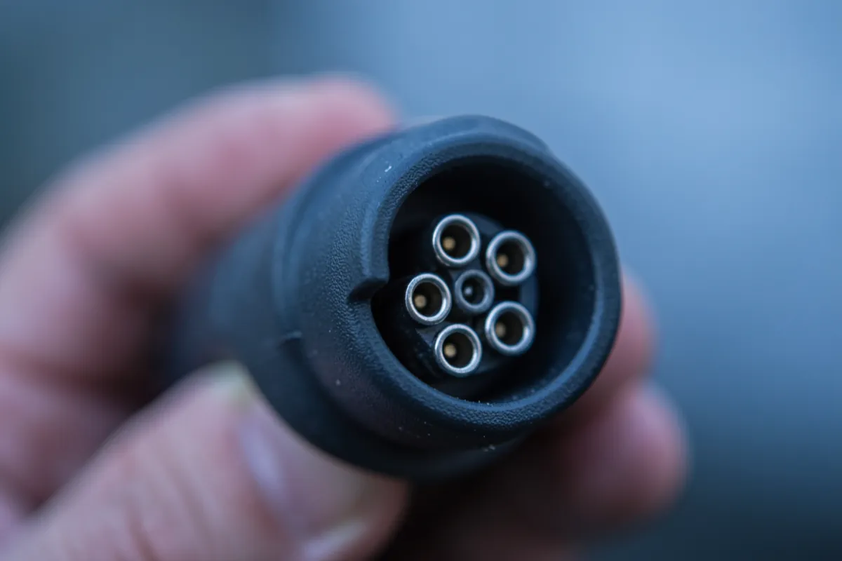 Lähikuva sähköauton latauskaapelin liittimestä ja sen metallisista kosketinpinneistä.