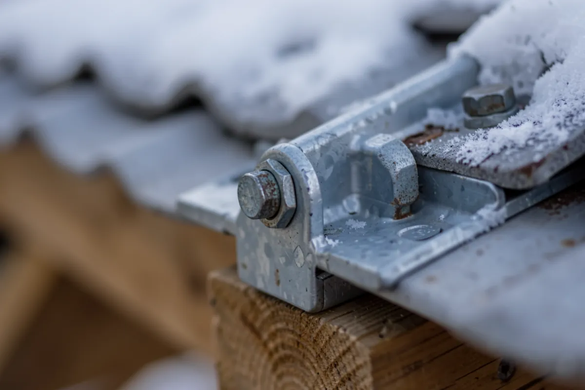Tuuliturbiinin järeä metallinen kiinnitysrakenne katon harjalla.